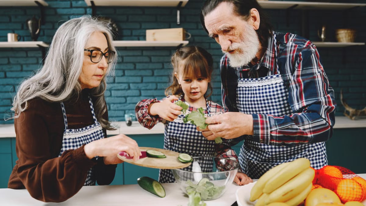 Elderly couple and young girl preparing salad in kitchen, emphasizing family connection.